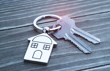 Key with silver house shaped pendant on wooden background