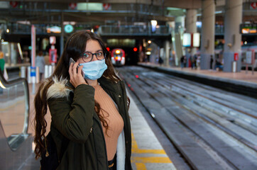 Mujer hablando con teléfono móvil con mascarilla en una estación de tren en Madrid
