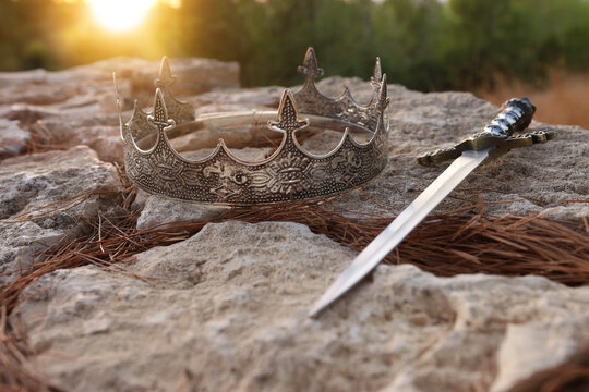 mysterious and magical photo of silver king crown and sword in the England woods over stone. Medieval period concept.