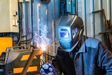 An electric and gas welder in an electromechanical workshop welds a metal structure at a mechanical...