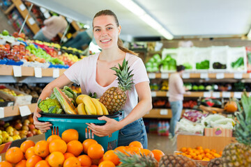 Obraz premium Cheerful woman standing with full shopping cart during shopping in fruit store