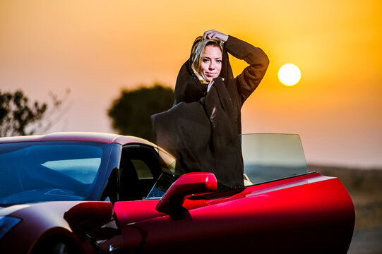 Arabic Way Dressed Yang Woman Posing In Red Car In Desert