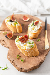 Bruschettas with figs, cream cheese, honey and microgreen on wooden board on white background. Side view, close up. Menu, recipe. Italian cuisine, healthy breakfast.