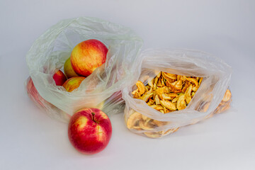 Red orange seasonal apples and yellow dried slices of apples in transparent plastic cellophane bags on white background. Fruit. Ecology concept