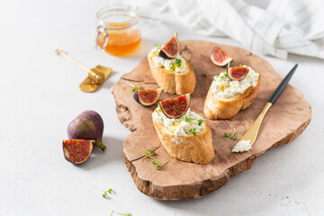 Sandwiches with ricotta, fresh figs, microgreen and honey on rustic wooden board over white backdrop, top view. Italian bruschetta recipe, menu. Healthy breakfast