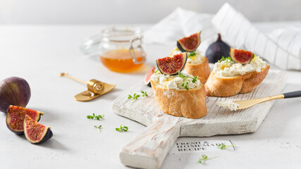 Fig, cream cheese and honey sandwiches. Canape or crostini with toasted baguette, cream cheese, figs and microgreen on a wooden board on white background. Italian recipe menu. Side view, close up