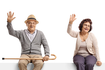 Fototapeta premium Elderly man and woman sitting on a blank billboard sign and waving at the camera