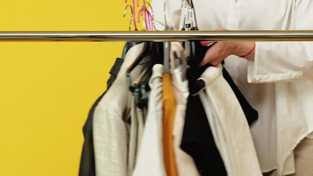 Seasonal sale. Female shopping. Capsule wardrobe. Ready-to-wear collection. Image consultant service. Female fashion stylist hands taking away clothes on hangers isolated on orange background.