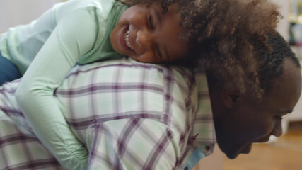 Happy black father giving piggyback ride to overjoyed little daughter.