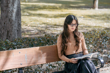 Mujer joven con un libro en la mano en un paisaje de otoño y sentada en un banco