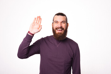 Fototapeta premium A photo of a young bearded cheerful man showing hello gesture and looking at the camera smiling