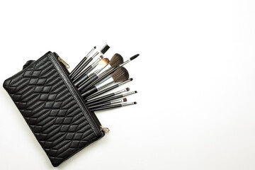 Fashion black handbag with a set of different make-up tools on white background. Typical handbag of a modern young lady with cosmetics