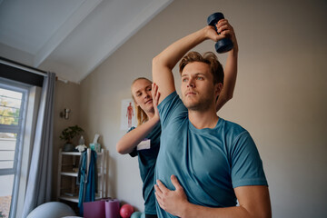 Physiotherapist instructing male patient correct exercise form with dumbbells