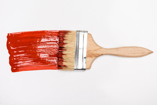 top view of paintbrush near colorful red paint brushstroke on white background