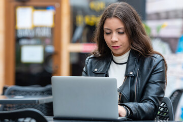 Portrait of a happy young woman relaxing in outdoor cafe and using a laptop
