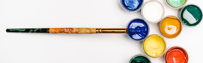 top view of colorful Gouache paints and paintbrush on white background, panoramic shot
