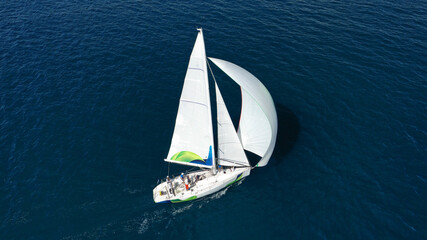 Fototapeta premium Aerial drone photo of beautiful white sailboat with wooden deck cruising in deep blue Aegean sea near Santorini island, Cyclades, Greece