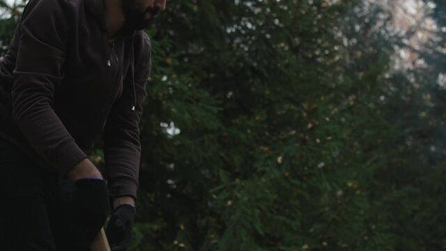 Young handsome man chops wood in the forest. A lumberjack chops birch logs for firewood.