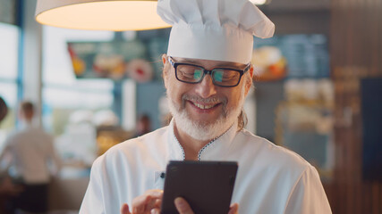 Portrait of mature male chef using digital tablet in modern fast food cafe