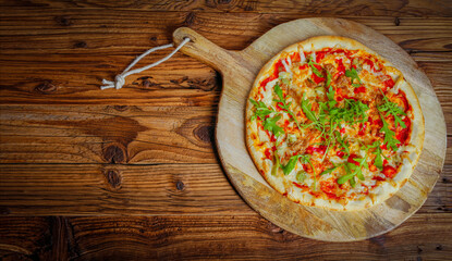 Hot freshly baked homemade pizza tuna sprinkled with arug. Old wood as a background . Copy space for text or description.