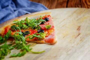 Freshly baked homemade ham pizza with black olives sprinkled with aruged on a wooden background.