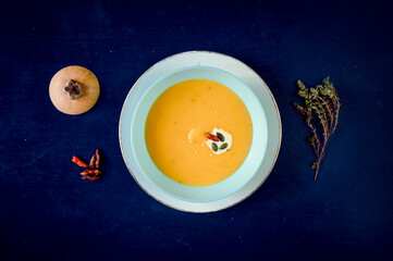 Spicy pumpkin cream soup with decorations and coffee in the background on a blue rustic table