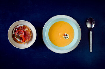 Spicy pumpkin cream soup with decorations and coffee in the background on a blue rustic table