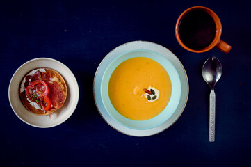Spicy pumpkin cream soup with decorations and coffee in the background on a blue rustic table