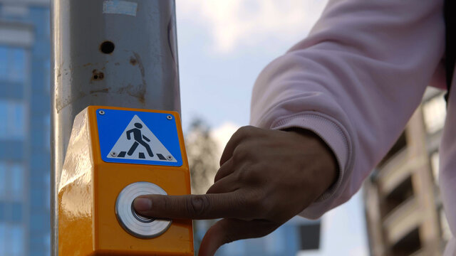 Close up of young afro guy on scooter pressing button of traffic light to safely cross road.