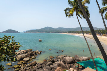 View of coastal rocks, palm trees and mountains on the horizon near Palolem beach in Goa, India