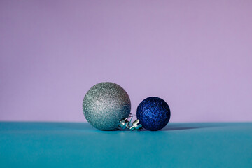 Christmas balls in blue and silver colors of different sizes are arranged in a row on a turquoise and pink background.