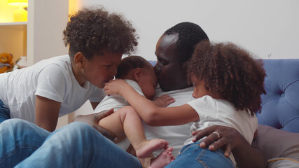 Happy african american single father with little children lying on bed.