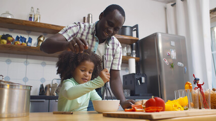Happy african father and daughter making dough for pizza having fun together in kitchen indoors.