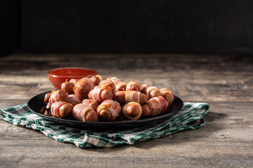 Pig in blankets. Sausages wrapped in smoked bacon on wooden table.Copy space	
