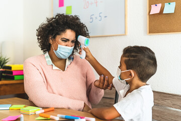 Child checkup temperature on teacher in classroom during corona virus pandemic - Healthcare medical and education concept