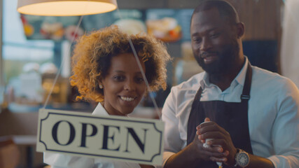 African cheerful small business owners smiling and turning open sign on cafe glass door