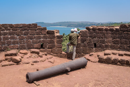 A man with a child next to an old cannon looking at the Indian ocean from the height of the former Portuguese fortress Cabo De Rama in Goa, India
