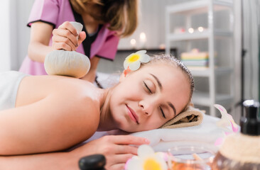 Obraz na płótnie Canvas Beautiful young woman lying and relaxing with having massage by herbal compress balls in therapy spa salon. Beauty of lady in spa salon getting therapy from thai massage of asian woman in spa resort.