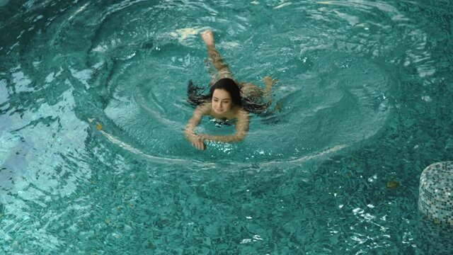 Relaxed woman enjoying vacation in spa. Charming girl swimming indoor pool.