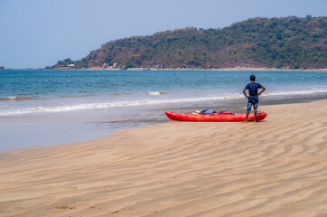 Fototapeta na wymiar A teenager next to a canoe looking at the ocean on a sandy beach in Goa, India