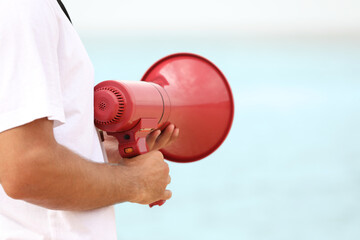 Male lifeguard with megaphone near sea, closeup