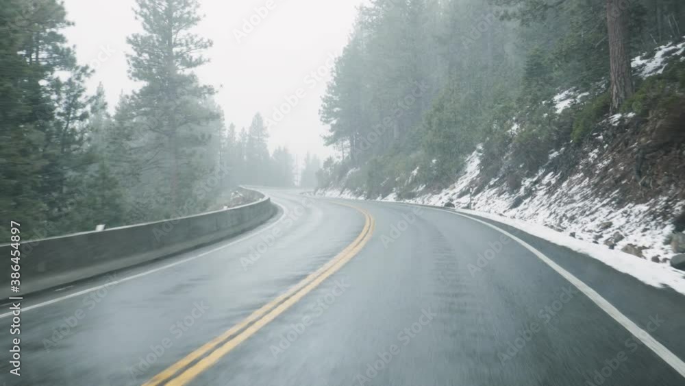 Sticker Driving on road with falling snow. Scenic view of snowy icy mountain road with pine trees. Danger travel conditions in winter, 4k