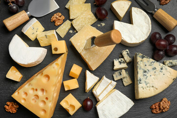 Cheese platter with specialized knives and fork on black table, flat lay