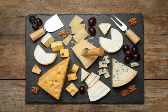Cheese platter with specialized knives and fork on wooden table, top view