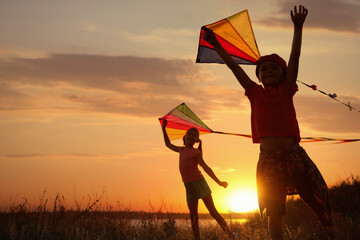 Cute little children playing with kites outdoors at sunset. Spending time in nature