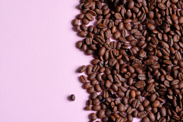 Roasted and aromatic Coffee beans on pink colored surface as background. Top view with and copy space for text. Macro photo of fresh arabica coffee beens.