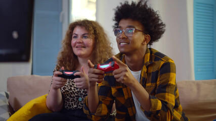 Cheerful diverse couple competing with each other in video games, holding joysticks and laughing