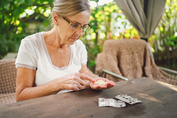 Senior old woman in glasses takes vitamins pills outdoors in garden. Healthcare aged people concept