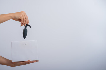 A woman folds a black anal plug into a paper bag on a white background. The concept of shopping in...