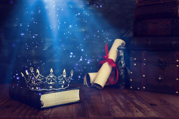low key image of beautiful queen/king crown, old books and feather quill ink pen over wooden table....